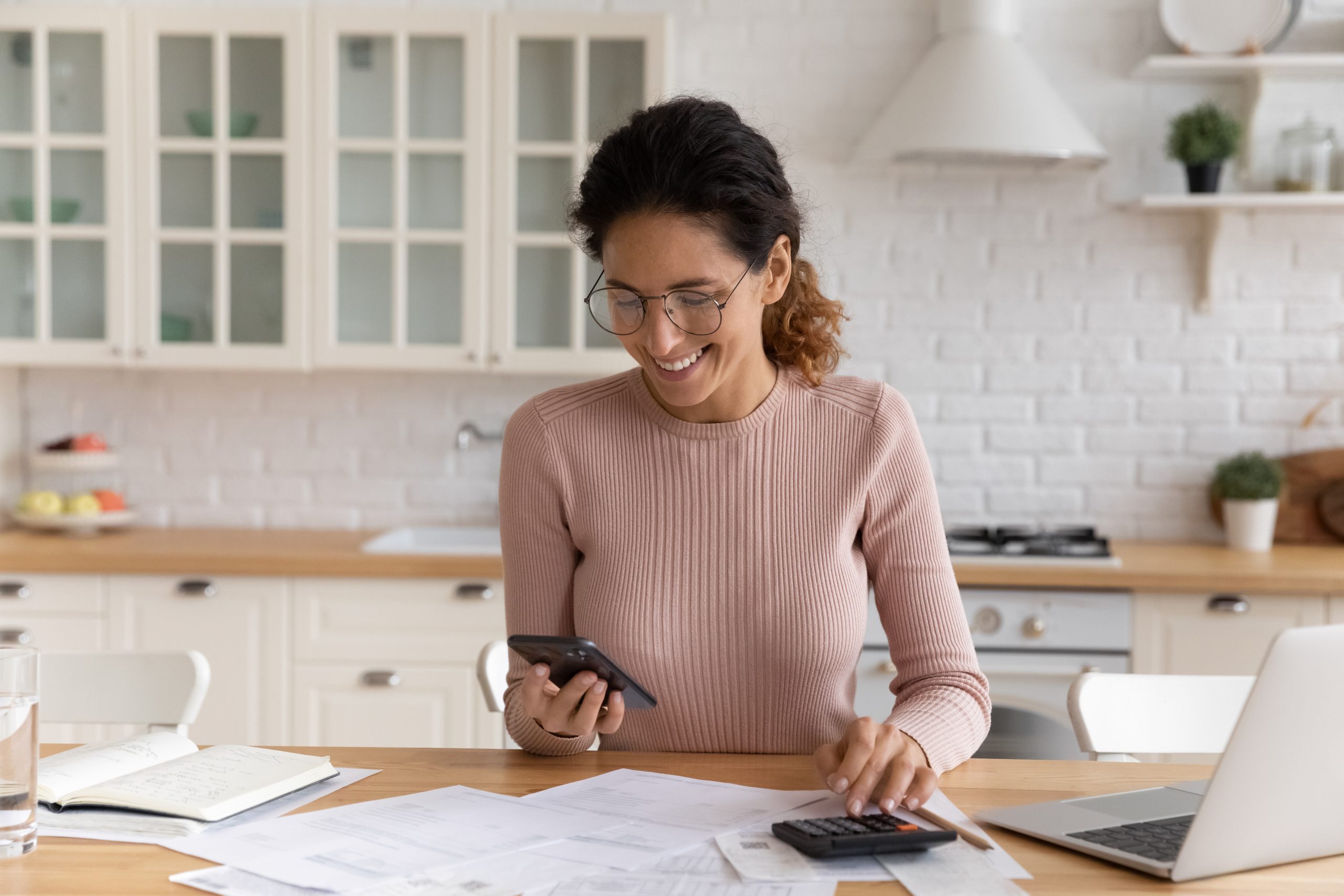 Comment financer sa formation en ligne avec INEAD. Jeune femme souriante analysant les financements possibles avec une calculatrice et des factures.