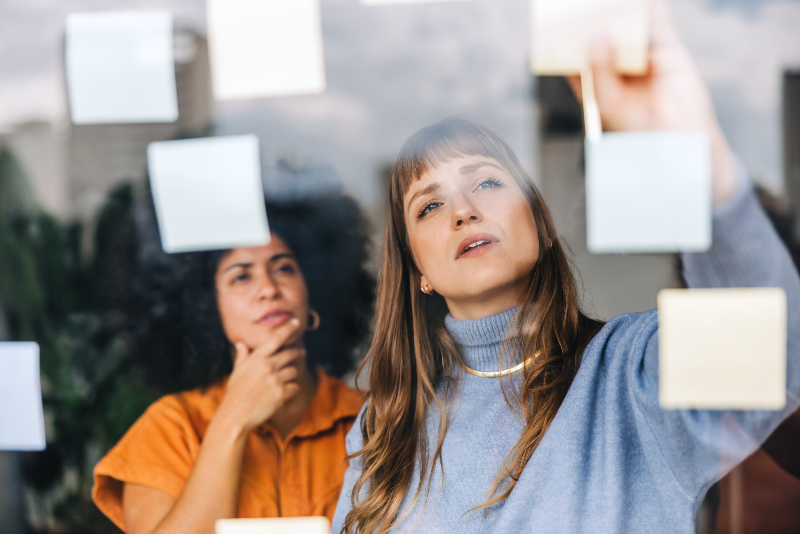 Présentation INEAD, école en ligne. Femmes en reflexion, conçevant les parcours de formation en s'aidant de post-it collés sur un tableau.